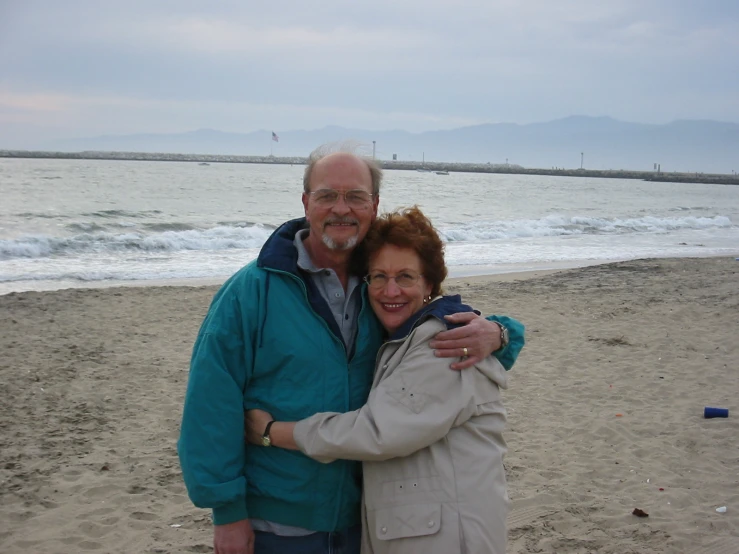 a man and woman standing on a beach next to the ocean