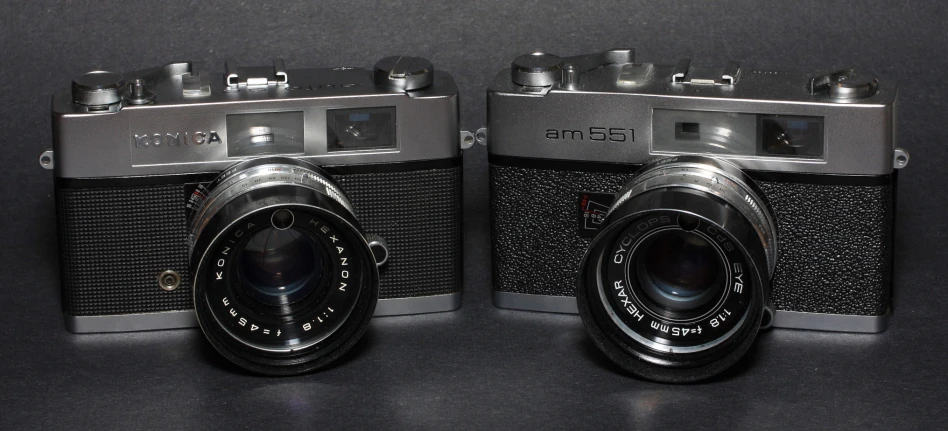 two old camera's sit side by side on a black surface