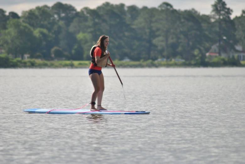 a young lady paddles across a lake with a paddle board