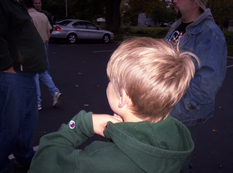 a little boy wearing a jean jacket standing next to a group of people