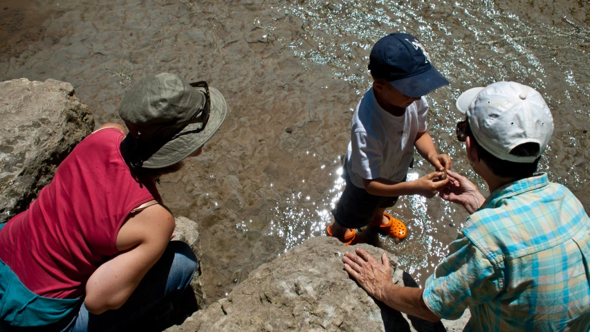 three people stand near rocks near a river