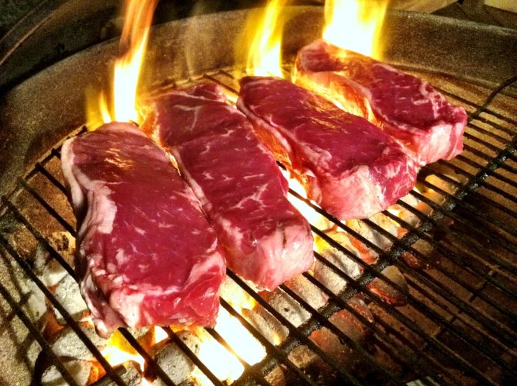 steaks cooking on a grill as flames spread over them