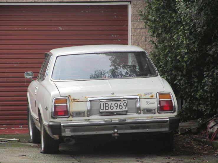 the back of an old white car in front of a garage