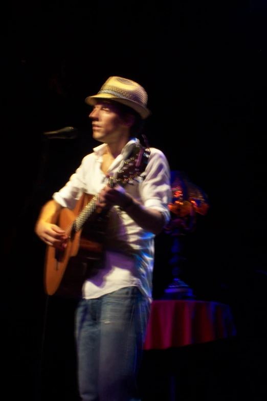 a man with a hat playing an acoustic guitar