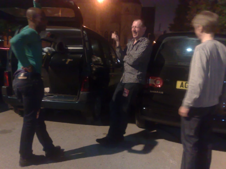 a group of young men standing next to a black car