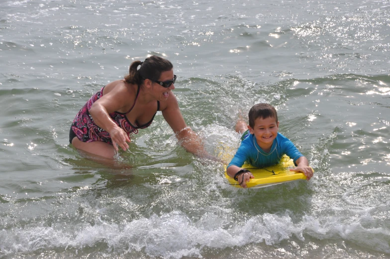 a woman teaching a child to ride a boogie board in the water