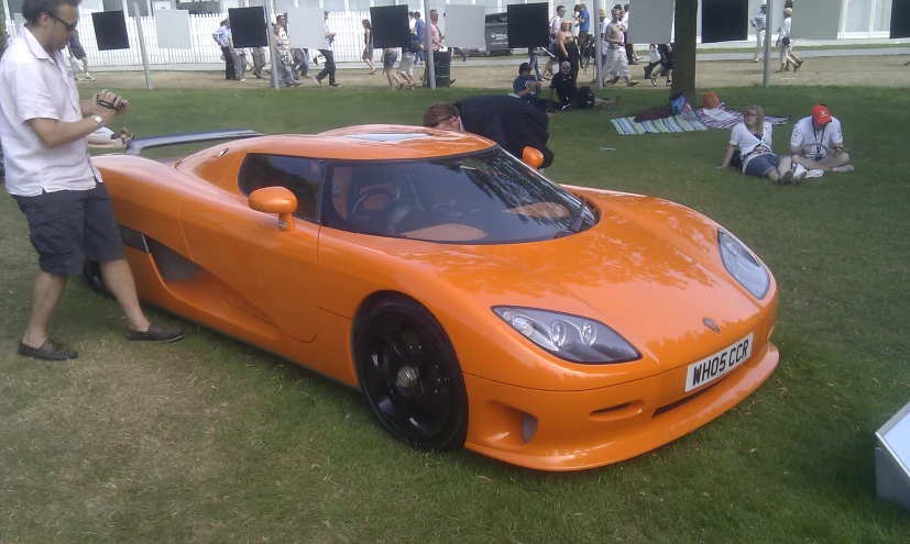 a man is standing next to a large orange sports car