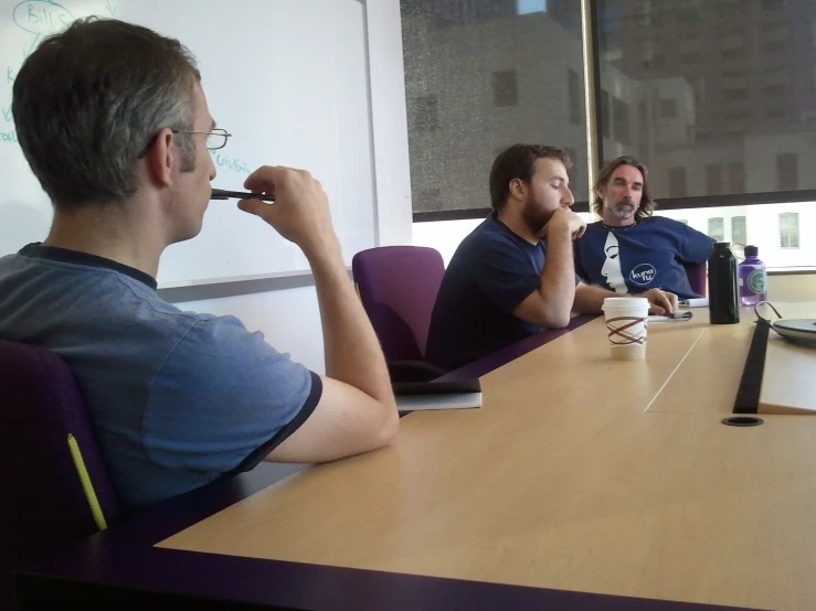 three men in blue shirts sitting at a conference table