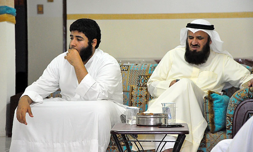 two men sitting on different chairs wearing long white clothing