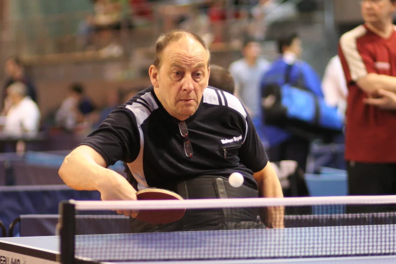 an older man playing ping pong at an indoor event