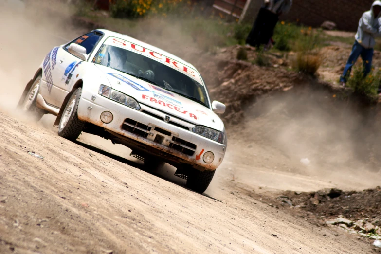 a silver rally car is driving down a dirt road