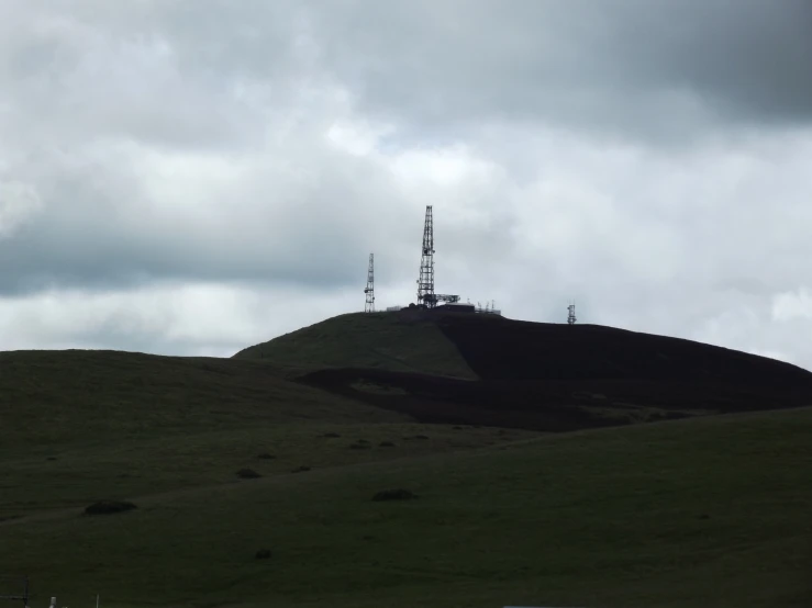 a dark hill under a cloudy sky with a antenna