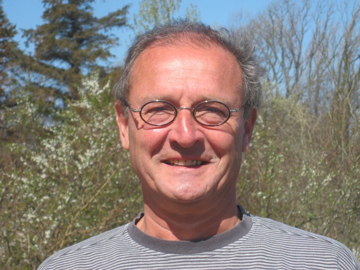 a man with glasses and a striped shirt smiling at the camera