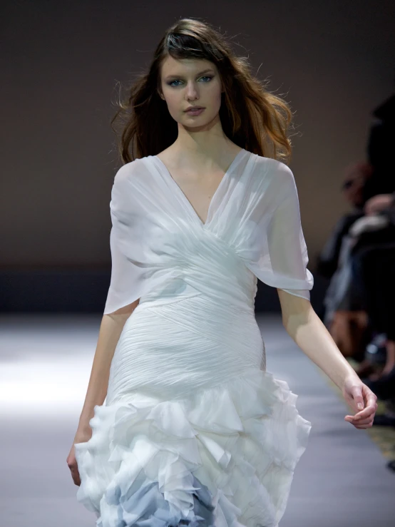 a model in a white dress walks down a runway