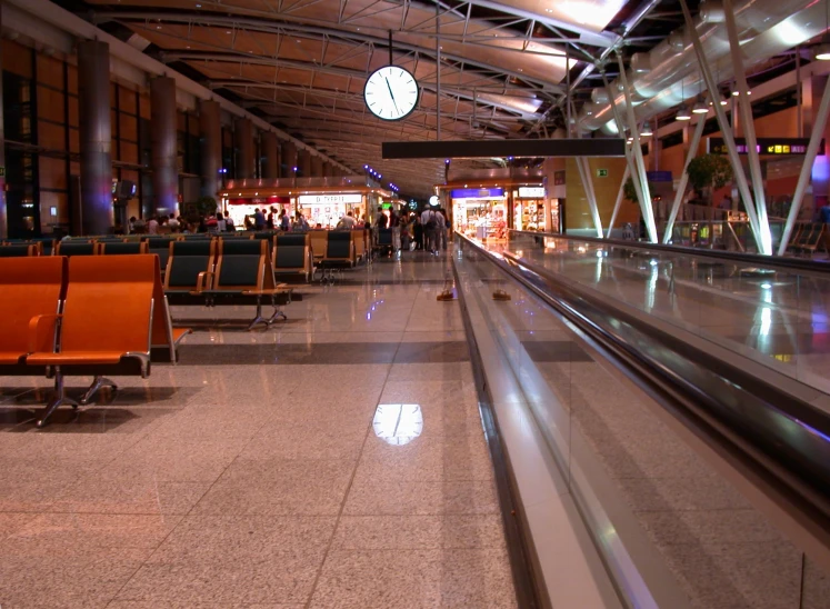 an empty baggage claim at an airport with seating and a large clock