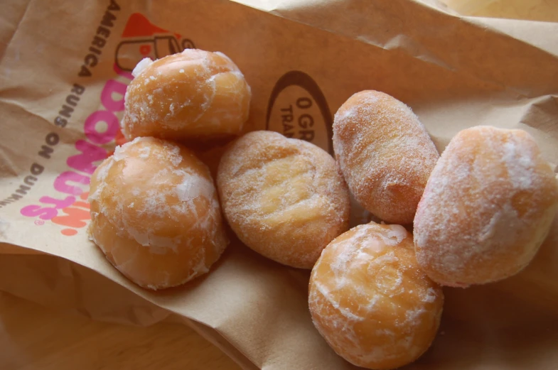 several sugar donuts sit in a brown paper bag