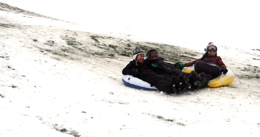 three people are in the snow on sleds