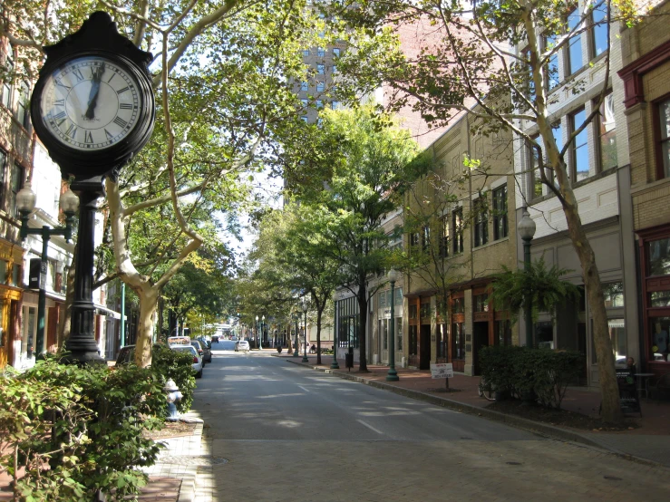 the clock is standing on the sidewalk in front of the buildings