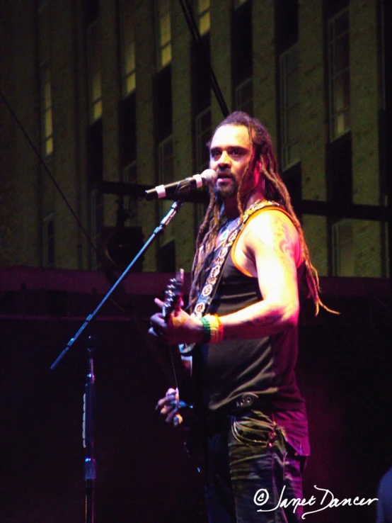 man with dread locks standing next to microphone in front of a microphone stand