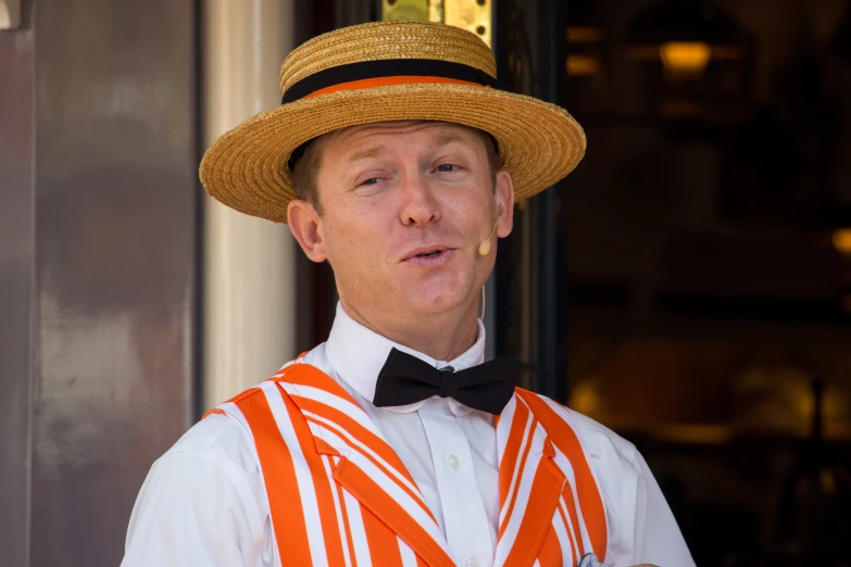 man with straw hat and striped vest standing by wall