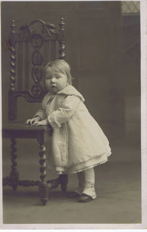 vintage pograph of toddler standing on chair with leg over side