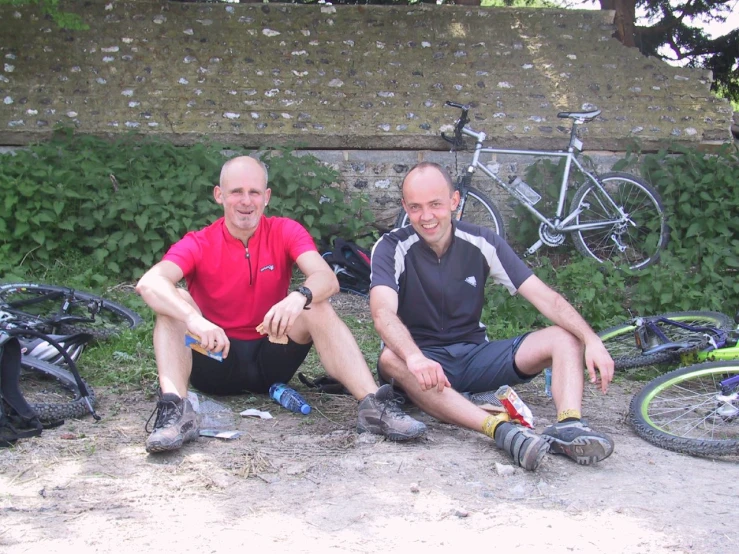 two men sitting next to each other with their bicycles