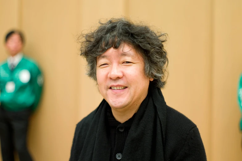 man in black jacket smiling while standing in front of two green wall panels