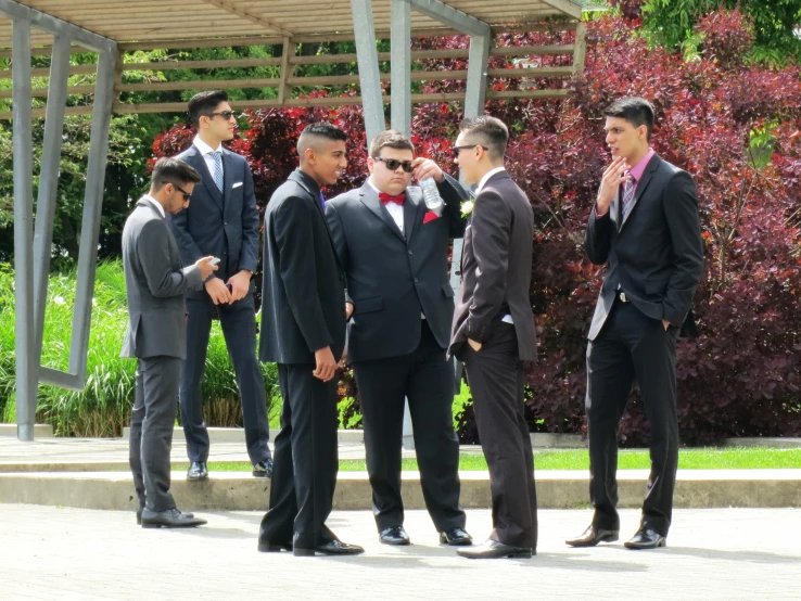 five men in suits stand in front of trees