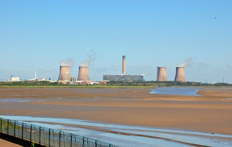 two smoke stacks towering over a lake and power station