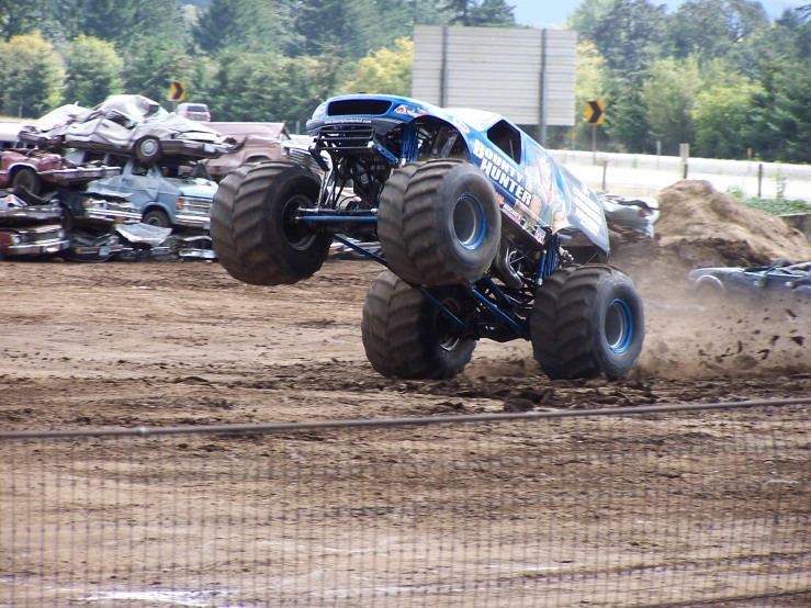 a large monster truck jumping over dirt with cars behind it