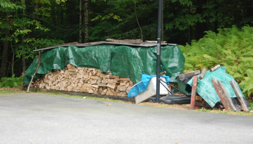 wood piled in the road and covering it with a green tarp