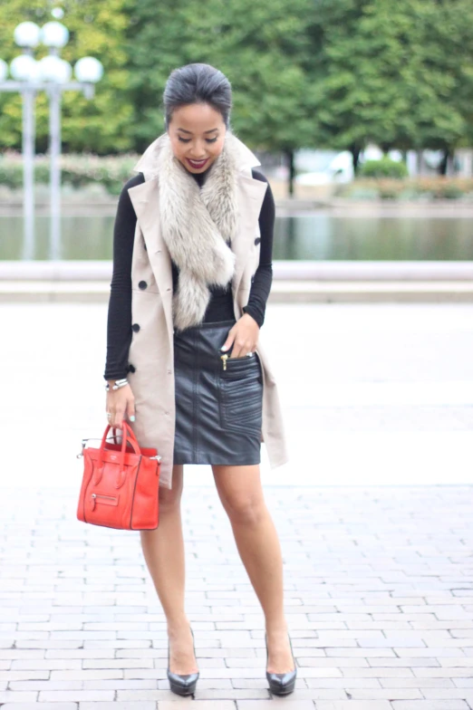 the woman is wearing a skirt and coat while holding a red purse