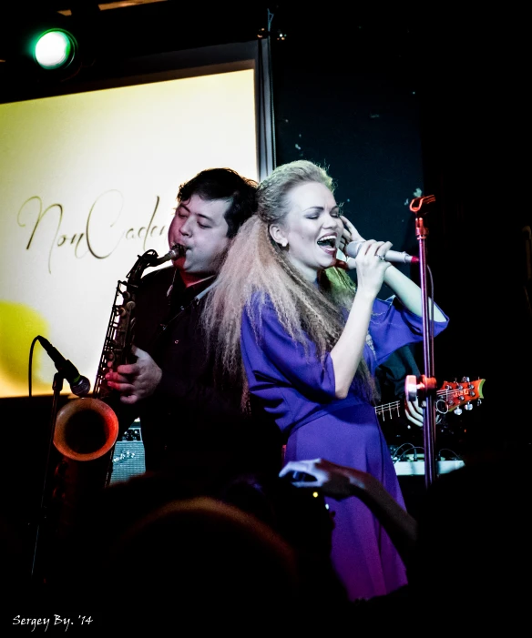 two people singing in front of a screen while holding saxophone