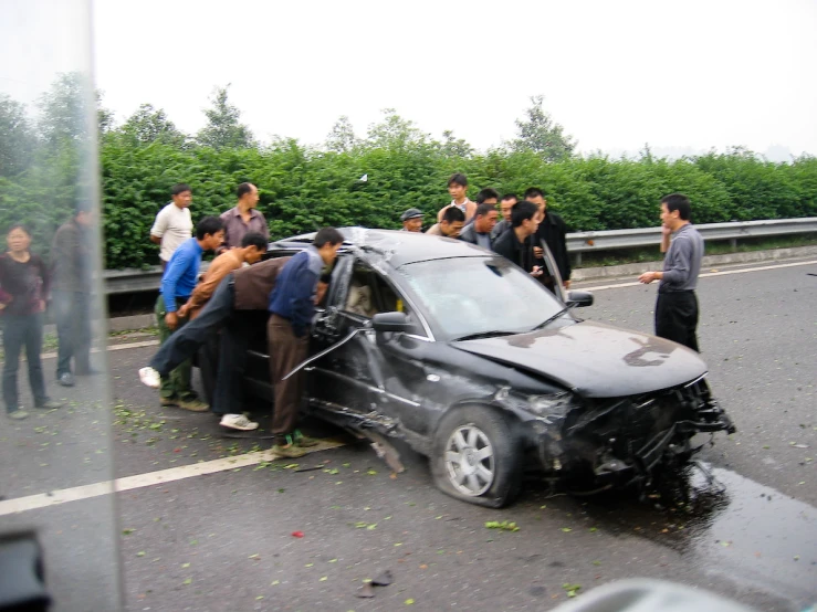 some people standing around the front of a car that has it's hood torn off