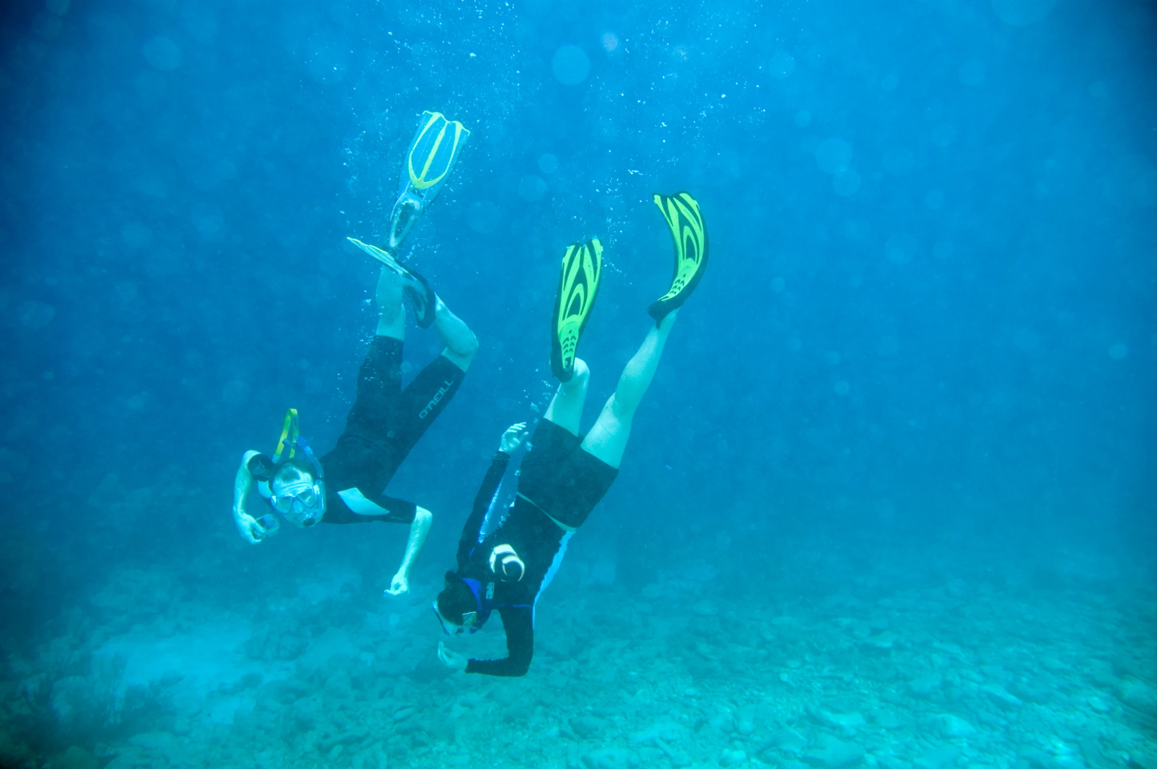 two people wearing black swimsuits and snorks, swimming underwater with their feet up