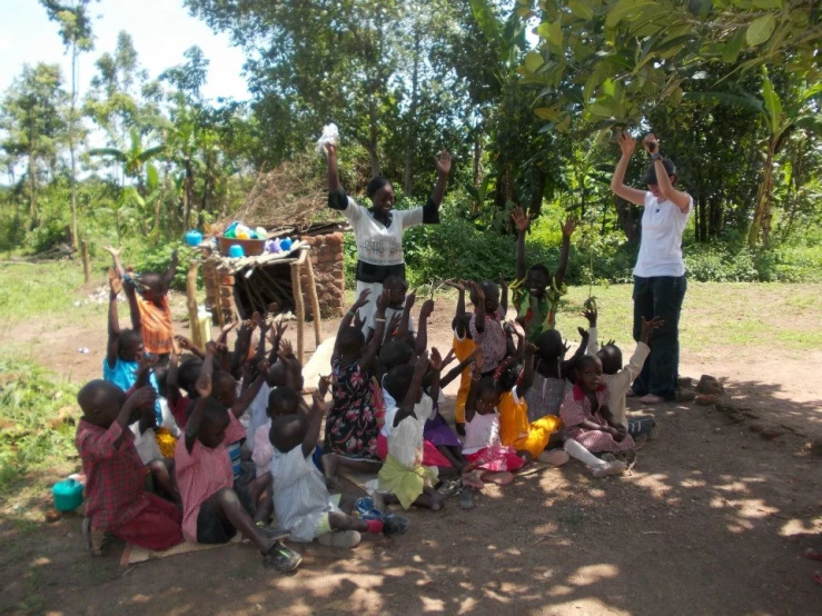 a group of children are sitting together and the men are holding up soing