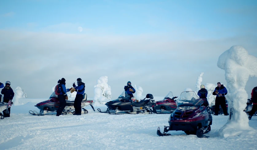 people riding skis on snow covered ground next to snow mobiles