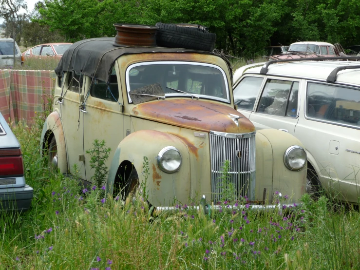 an old car with surfboards on top is parked near some cars