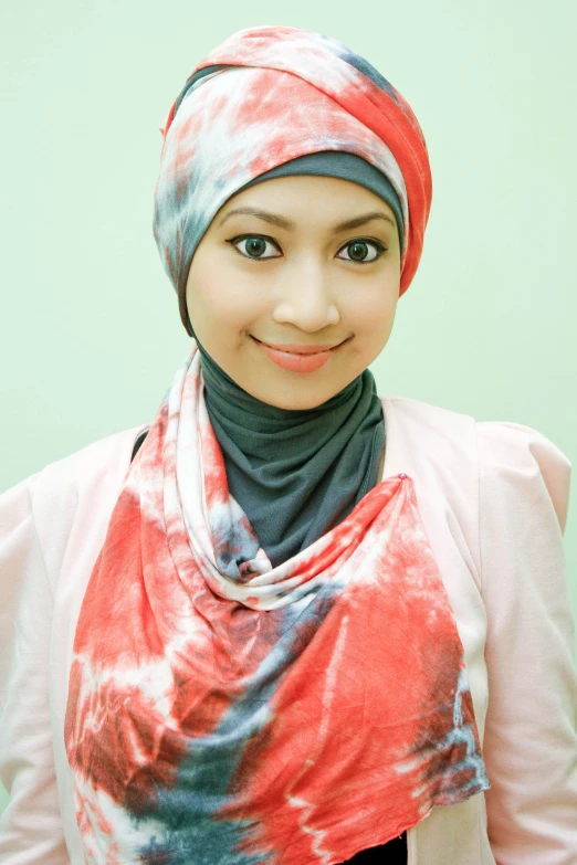 a girl with a red tie dyed hijab smiles into the camera