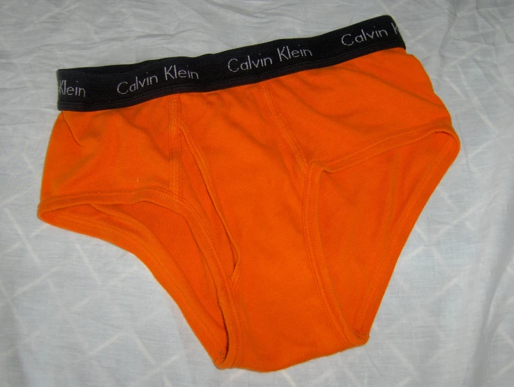 two pairs of orange underwear laying on top of a bed
