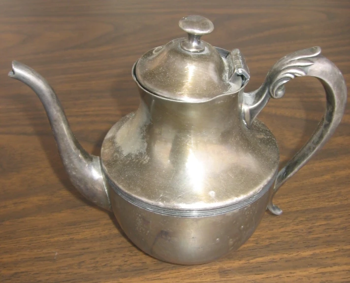 an antique silver tea pot on wooden table