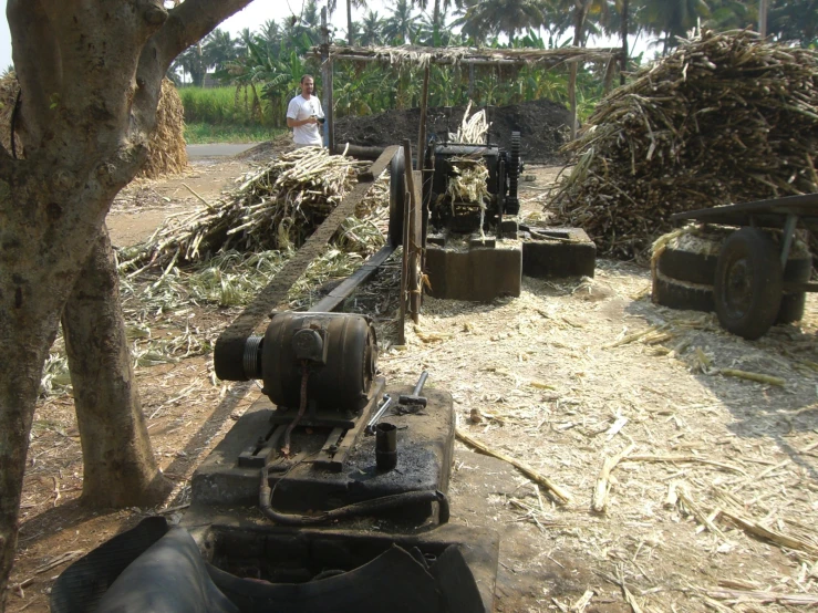 a machine sits near a pile of hay and a man walking past