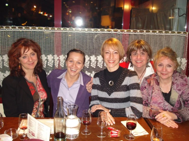 four ladies sitting at a table in a restaurant with their arms around each other