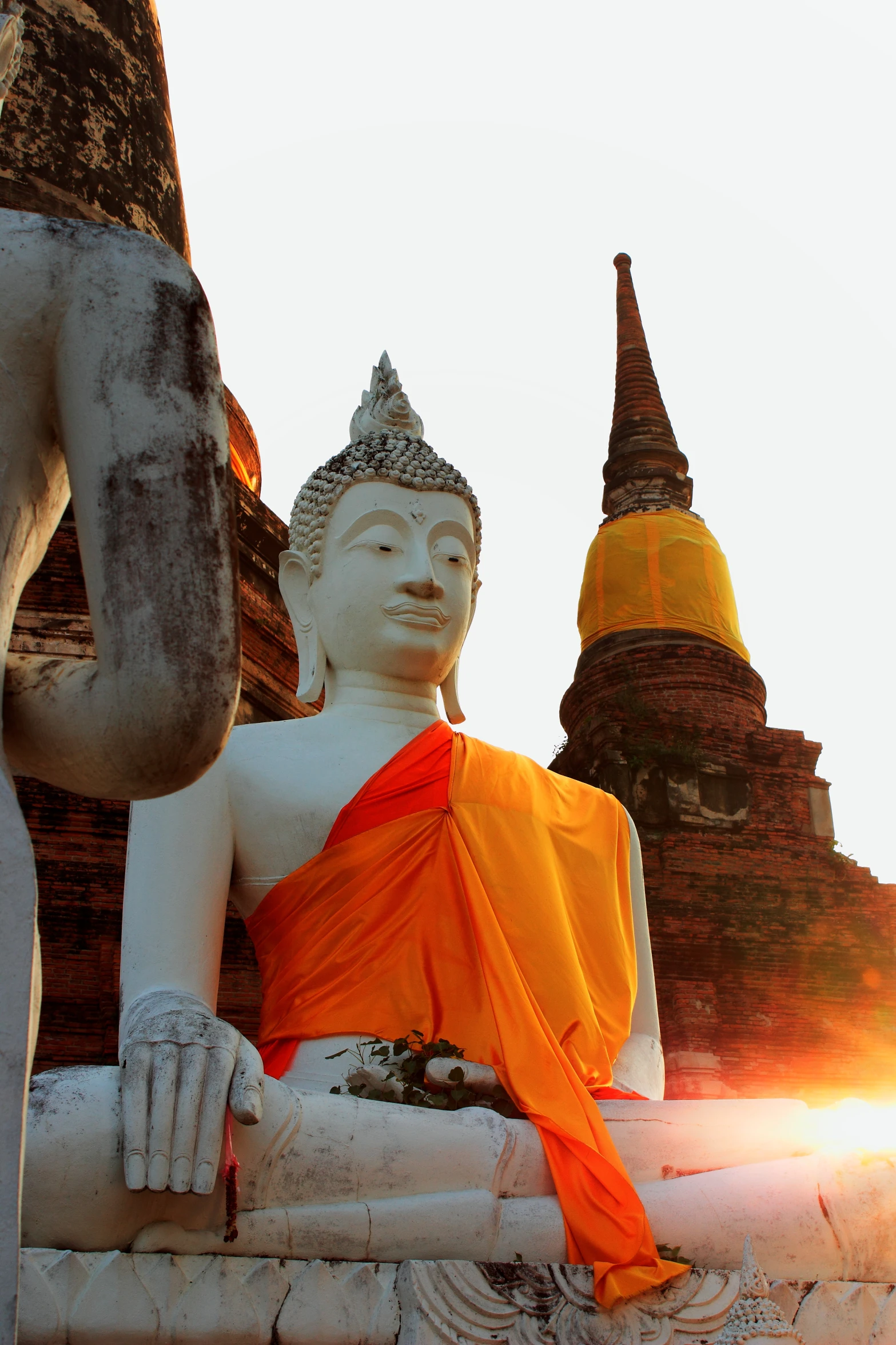 statue of buddha and sun setting over three different sized pagodas