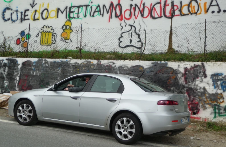 a silver car parked by a graffiti filled wall