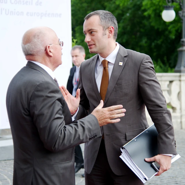 two men in suits talking to each other outside