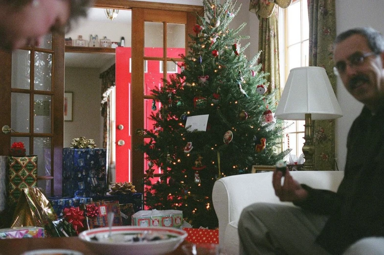 two men in a living room setting by a christmas tree