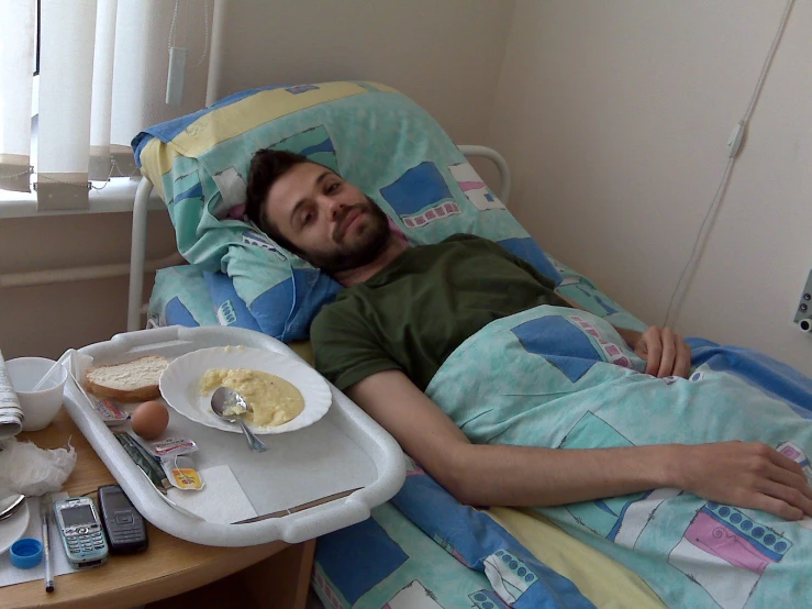 man lying in a hospital bed with a tray of food