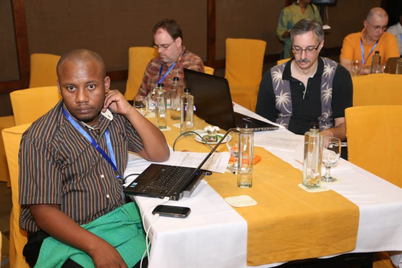 the man is on his laptop at the table with his friends