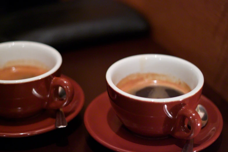 a red cup and saucer with milk sitting on a table